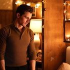 Kein Text. Ein nachdenklicher Mann in einem warm beleuchteten Raum mit Lichterkette und Schneekugeln auf Regalen.