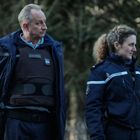 Zwei Personen in Uniformen mit "GENDARMERIE"-Schriftzug stehen nebeneinander, umgeben von einem bewaldeten Hintergrund.