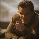 Ein Mann in braunem Sakko sitzt an einem Tisch in einem gedämpften Raum und lächelt freundlich.