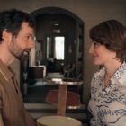 Eine Frau und ein Mann stehen sich in einem gemütlichen Raum lächelnd gegenüber.