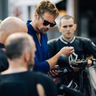 Fünf Männer stehen zusammen, einer hält ein Smartphone, ein anderer eine Schale schwarzer Oliven. Alle in Motorradkleidung.