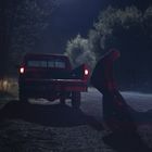 Ein Mädchen in rotem Regenmantel und -stiefeln sitzt auf einem Tierkopf, hält einen Stock und isst Trauben.