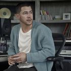 Ein Mann in einem Musikstudio sitzt vor einem Keyboard, Blick nach rechts. Im Hintergrund Regale mit Büchern und Gitarren.