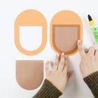 Zwei orangene Papierformen, U-förmig, mit durchsichtigen Einsätzen. Hände und eine Flasche Bastelkleber sind sichtbar.