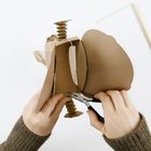 Hände biegen Draht an einem braunen Pappmodell; Hintergrund ist weiß. Tools sind Drahtschneider und Zange.