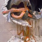 Eine monströse Kreatur durchbricht eine Mauer, mit langen, orangenen Tentakeln und tropfender, roter Farbe.