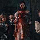 Fünf Personen in mittelalterlicher Kleidung, ernst und kampfbereit. Eine Frau in Rot ist blutverschmiert.