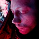 Ich kann keine Texte im Bild erkennen. Ein Mann, beleuchtet von pinken und blauen Lichtern, mit geschlossenen Augen.