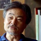 Es gibt keine erkennbaren Texte. Ein Mann mittleren Alters mit grauen Haaren und Bart, Hintergrund unscharf mit Büchern.