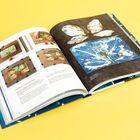 Text: "Wet Process with Spice Dyes". Geöffnetes Buch zeigt Bastelprojekte, Hände färben Stoff. Hintergrund in Gelb.