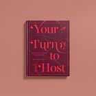 Text: "Your Turn to Host: A Guide to Great Parties and Gatherings, Amber Mayfield Hewett." Buch mit rotem Cover und Verzierung.