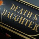Text: "DEATH'S DAUGHTER" in goldener Schrift auf schwarzem Hintergrund, verzierte Ränder und florales Detail.