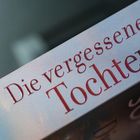 "Die vergessene Tochter" steht in roten Buchstaben auf einem Buchrücken, unscharfer Hintergrund.