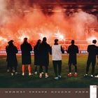 09 2027, September. Menschen betrachten brennende Fackeln im Stadion, während Rauch die Tribünen füllt.