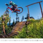 "9" und Kalendertage darunter. Ein Radfahrer springt mit einem Mountainbike über eine Rampe in einer Waldlandschaft.