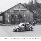 "Auto-Reparatur" ist auf einem Schild über einer Holzhütte zu sehen. Ein VW Käfer steht davor. Unten sind Kalendertage: "9".