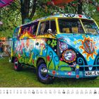 Kennzeichen: WAK-E 69. Ein bunter, mit Blumen bemalter VW-Bus steht auf einer Wiese unter Bäumen.