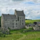 Kein Text vorhanden. Ein altes Steingebäude, umgeben von grünen Wiesen und einigen Bäumen, unter einem bewölkten Himmel.