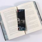 Seiten aus einem Buch sind offen, mit Text. Ein Lesezeichen zeigt ein Bild eines Hauses und Blumen.