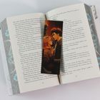 Ein Buch zeigt eine geöffnete Doppelseite, auf der ein illustriertes Lesezeichen mit zwei Figuren liegt.