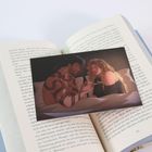 Ein offenes Buch mit einem Foto darin. Die Illustration zeigt eine Frau und einen Mann mit Schlangentattoo im Bett.