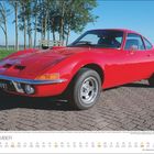 Text: "SEPTEMBER". Roter Sportwagen auf Straßenpflaster, im Hintergrund grüne Wiese und Bäume.