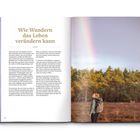 "Wie Wandern das Leben verändern kann" steht groß als Überschrift. Eine Person mit Rucksack blickt in einen Regenbogen im Wald.
