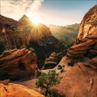 Keine Texte erkennbar. Strahlende Sonne über einer spektakulären Canyon-Landschaft mit roten Felsen und üppiger Vegetation.