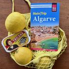 "Mein|Trip Algarve" auf einem Reiseführer mit Strandfoto. Daneben Zitronen und eine Sardinenbüchse "TRICANA".