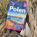 "Polen Ostseeküste und Masuren. Reiseführer für individuelles Entdecken." Ein Reiseführer liegt im Gras, daneben ein Miniaturboot.