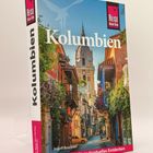 "KOLUMBIEN" steht groß auf einem Reiseführer. Darunter malerische Straßenansicht mit bunten Häusern und Pflanzen.