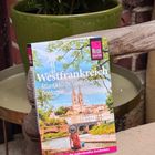 "Westfrankreich: Atlantikküste, Loire, Charentes, Dordogne", Reiseführer. Ein Buch liegt auf einem Holzstuhl, Hintergrund grüne Pflanze.