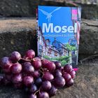 Ein Reiseführer mit "Mosel vom Dreiländereck bis Koblenz" vor fliederfarbenen Trauben auf Natursteintreppe.