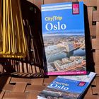 „CityTrip Oslo“, Reiseführer mit Stadtansicht. Im Vordergrund gelbe Wäscheklammern auf geflochtenem Untergrund.