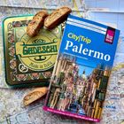 Reiseführer "CityTrip Palermo", eine grüne Dose mit "Gadeschi", darunter eine Stadtkarte, oben liegen Kekse.
