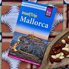 Reiseführer "Insel|Trip Mallorca", zeigt Küste mit Leuchtturm, liegt auf gemustertem Tuch, daneben Mandeln auf Fischbrett.