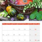 09 2027. Ein Korb mit Dahlien, Kürbissen, Blumen und grünen Blättern steht auf einem Holztisch. Darunter ein Kalender.