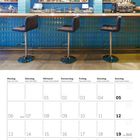 Kalender für September 2027 mit Bar, blauen Fliesen und drei schwarzen Barhockern, Mittagssonne scheint herein.