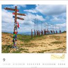 Wegweiser mit Beschriftungen zu Orten; im Hintergrund Metall-Silhouetten von Menschen und Pferden auf einem Hügel unter blauem Himmel.