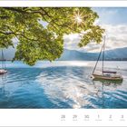 Juni/Juli, Tegernsee in Oberbayern. Zwei Segelboote, ruhiges Wasser, Berge im Hintergrund, Sonnenlicht durch Baumkronen.