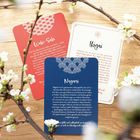 Drei Karten mit den Titeln "Wabi-Sabi", "Ikigai" und "Nagomi" sind auf einem Holztisch mit Kirschblüten dekoriert.