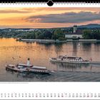 Parallelfahrt vor Friedrichshafen. Zwei Schiffe fahren auf einem See, dahinter eine Kirche und bewaldete Ufer.