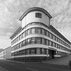 Text "carpet corner". Historisches Gebäude mit runden Ecken und vielen Fenstern, gepflasterte Einfahrt, wolkiger Himmel.