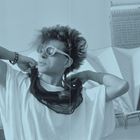 Ich kann den Text im Bild nicht erkennen. Ein Mensch trägt eine Sonnenbrille und posiert lässig in einer urbanen Umgebung.