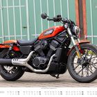 Text: "HARLEY DAVIDSON" und "SEPTEMBER". Rote Harley-Davidson-Motorrad vor grüner Wand auf Kopfsteinpflaster.