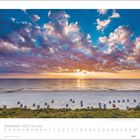 September 2027 | Am Meer. Ein Sonnenuntergang über einem Strand mit verstreuten Strandkörben und einem dramatischen Wolkenhimmel.