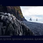 07 Juli. Kalenderansicht. Ein schwarzer Strand in Island mit markanten Felsen und tosender See im Hintergrund.