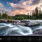 „Skandinavien 09. Stromschnellen bei Kvikkjokk (Schweden)“. Fluss mit Felsen, umgeben von Wäldern und Bergen bei Sonnenuntergang.