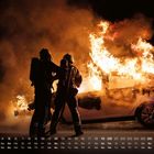 Kalender im September. Feuerwehrleute stehen vor brennendem Auto in Nacht, Flammen lodern, dichte Rauchwolken.