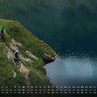 Kalender mit Monatstagen unten. 
Zwei Radfahrer fahren auf einem schmalen Pfad an einem Bergsee entlang.